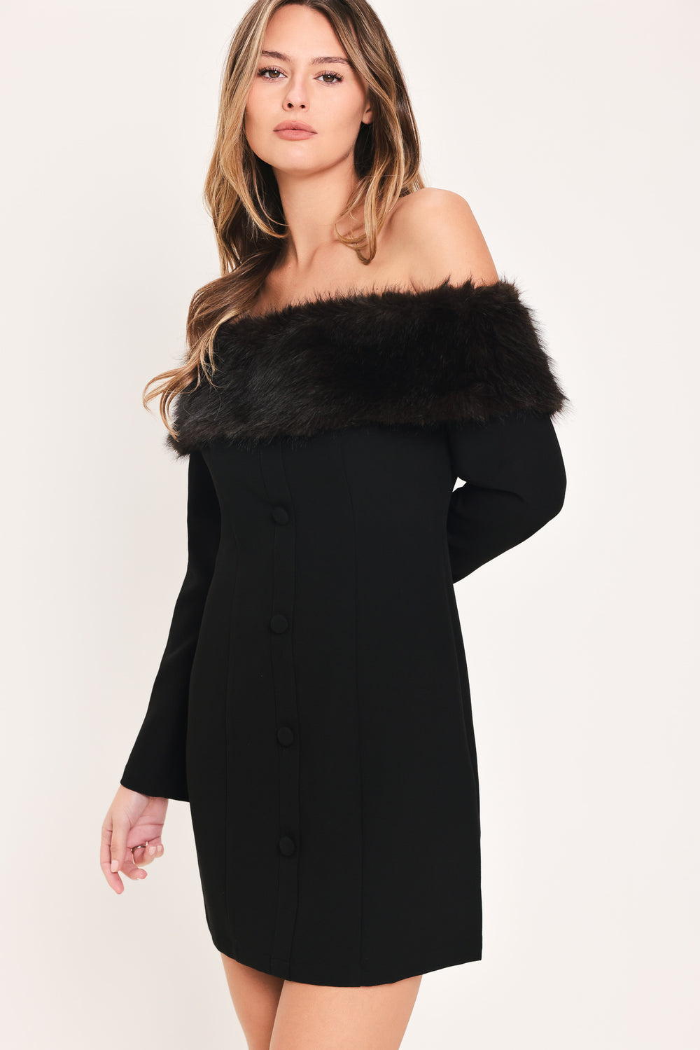A woman modeling a black off-the-shoulder long-sleeve mini dress with a wide black faux-fur collar and a front button closure | Flying Tomato