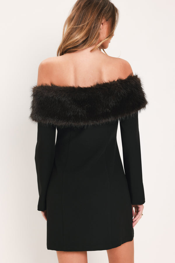 A woman modeling a black off-the-shoulder long-sleeve mini dress with a wide black faux-fur collar and a front button closure | Flying Tomato