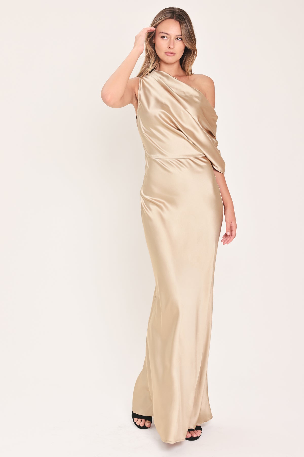A woman modeling a floor-length, one-shoulder satin gown in a champagne beige color | Flying Tomato