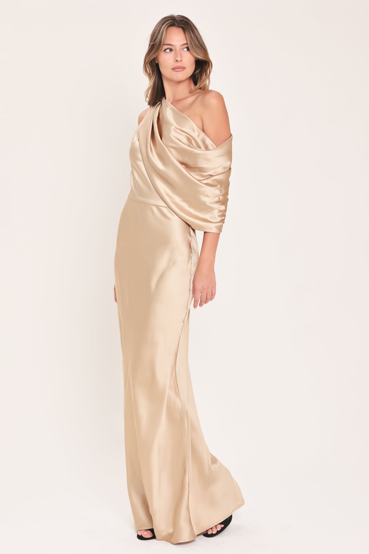 A woman modeling a floor-length, one-shoulder satin gown in a champagne beige color | Flying Tomato
