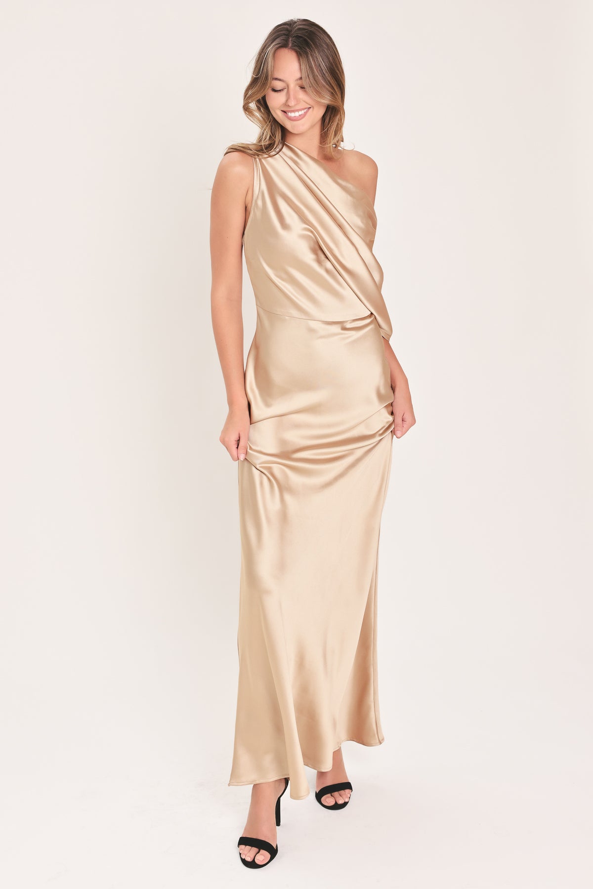 A woman modeling a floor-length, one-shoulder satin gown in a champagne beige color | Flying Tomato
