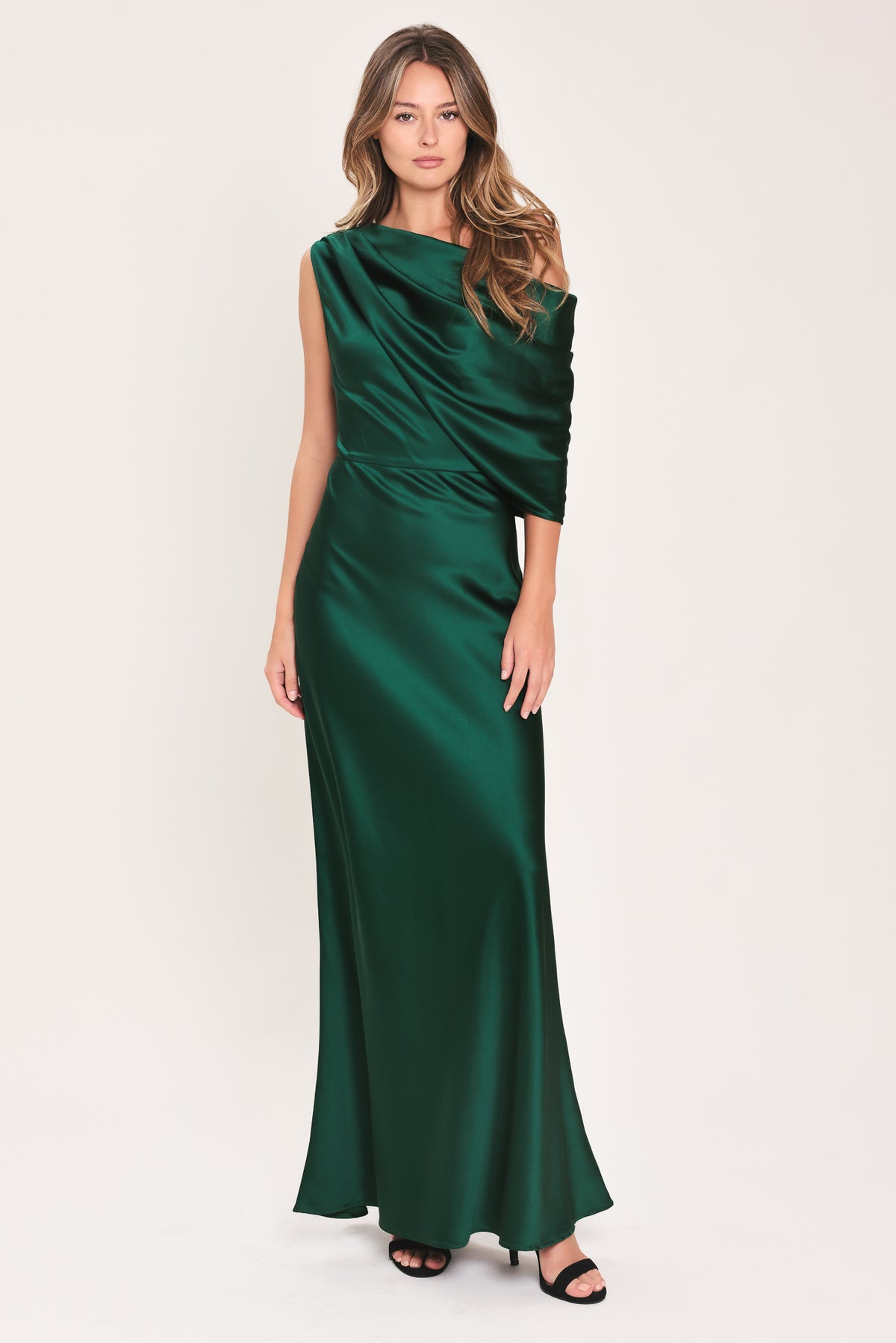 A woman modeling a floor-length maxi emerald green satin dress with draped asymmetrical detailing and a draped shoulder design | Flying Tomato