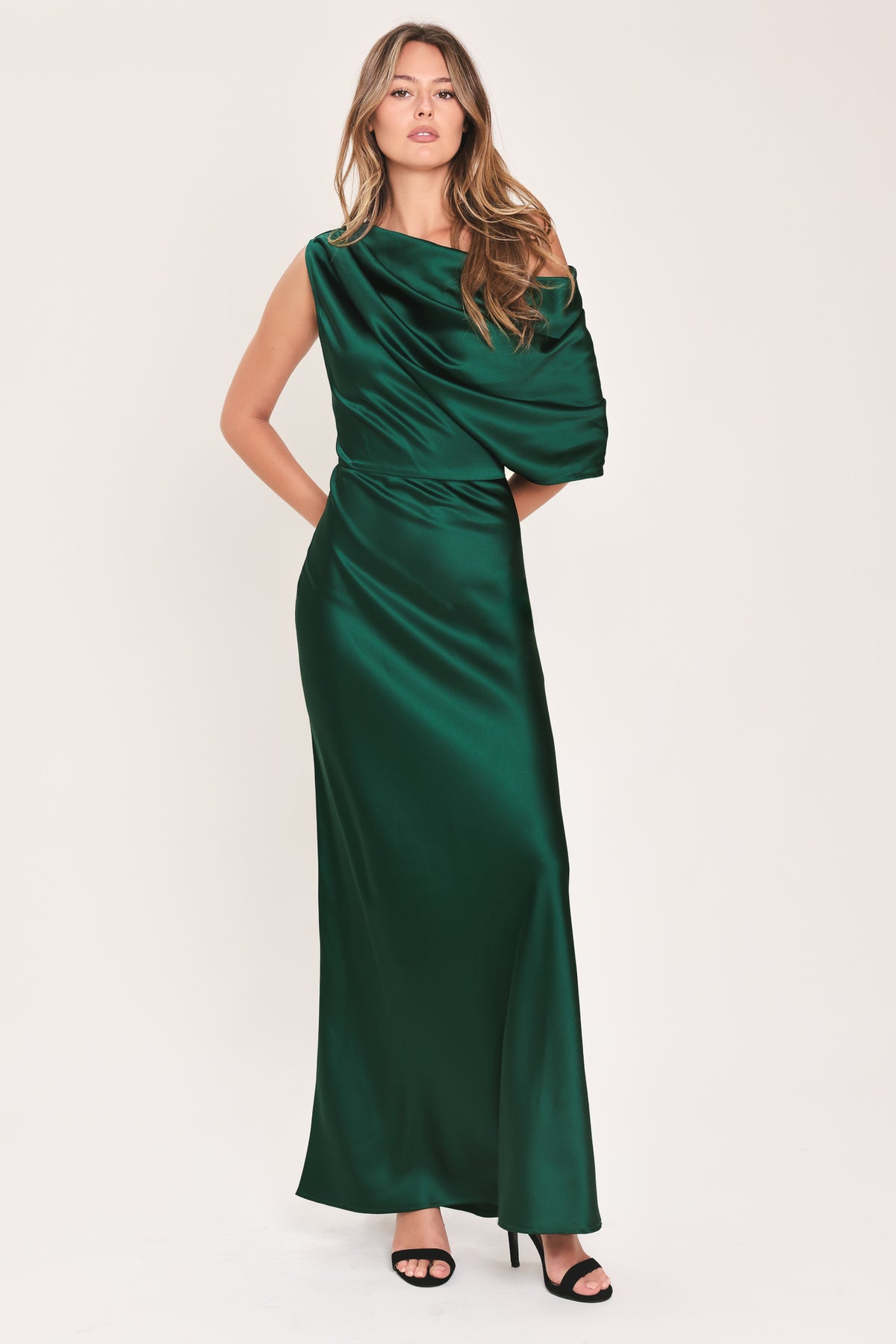 A woman modeling a floor-length maxi emerald green satin dress with draped asymmetrical detailing and a draped shoulder design | Flying Tomato