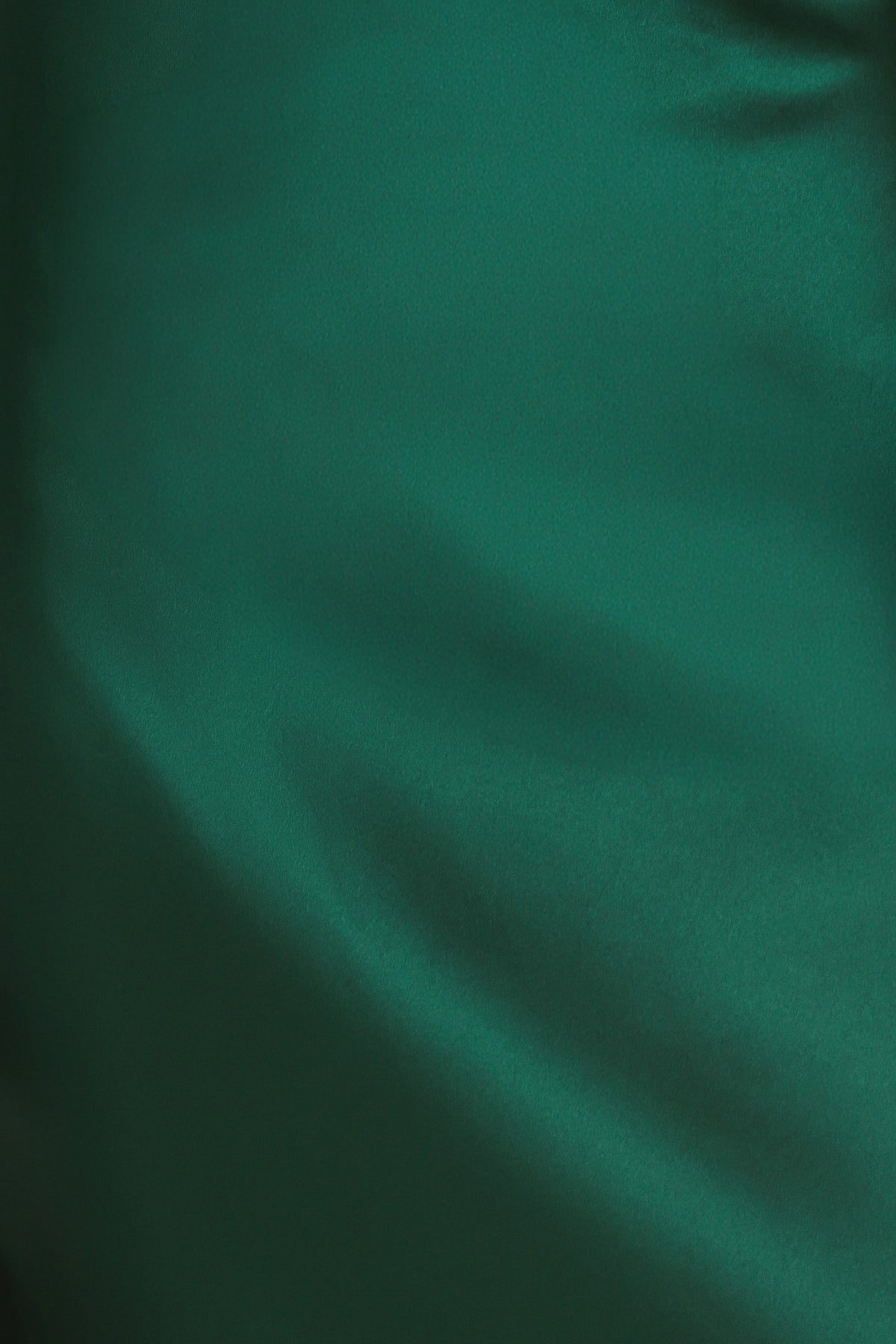 A woman modeling a floor-length maxi emerald green satin dress with draped asymmetrical detailing and a draped shoulder design | Flying Tomato