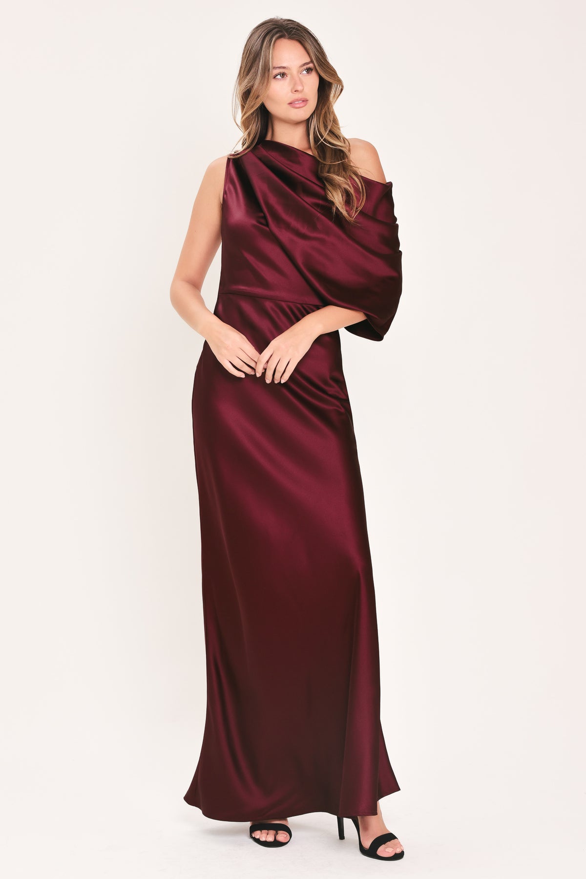 A woman modeling a floor-length maxi draped satin gown in deep burgundy wine, featuring an asymmetrical draped neckline and one sleeve | Flying Tomato