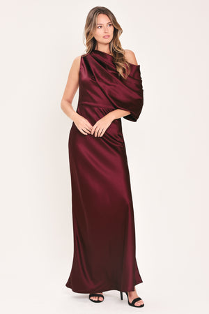 A woman modeling a floor-length maxi draped satin gown in deep burgundy wine, featuring an asymmetrical draped neckline and one sleeve | Flying Tomato