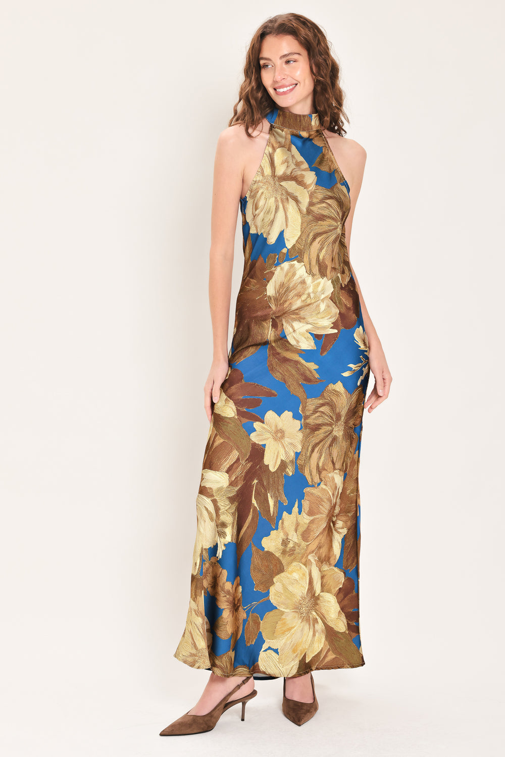 Woman wearing a sleeveless blue satin maxi dress with a mock halter neckline and gold and brown floral pattern | Flying Tomato
