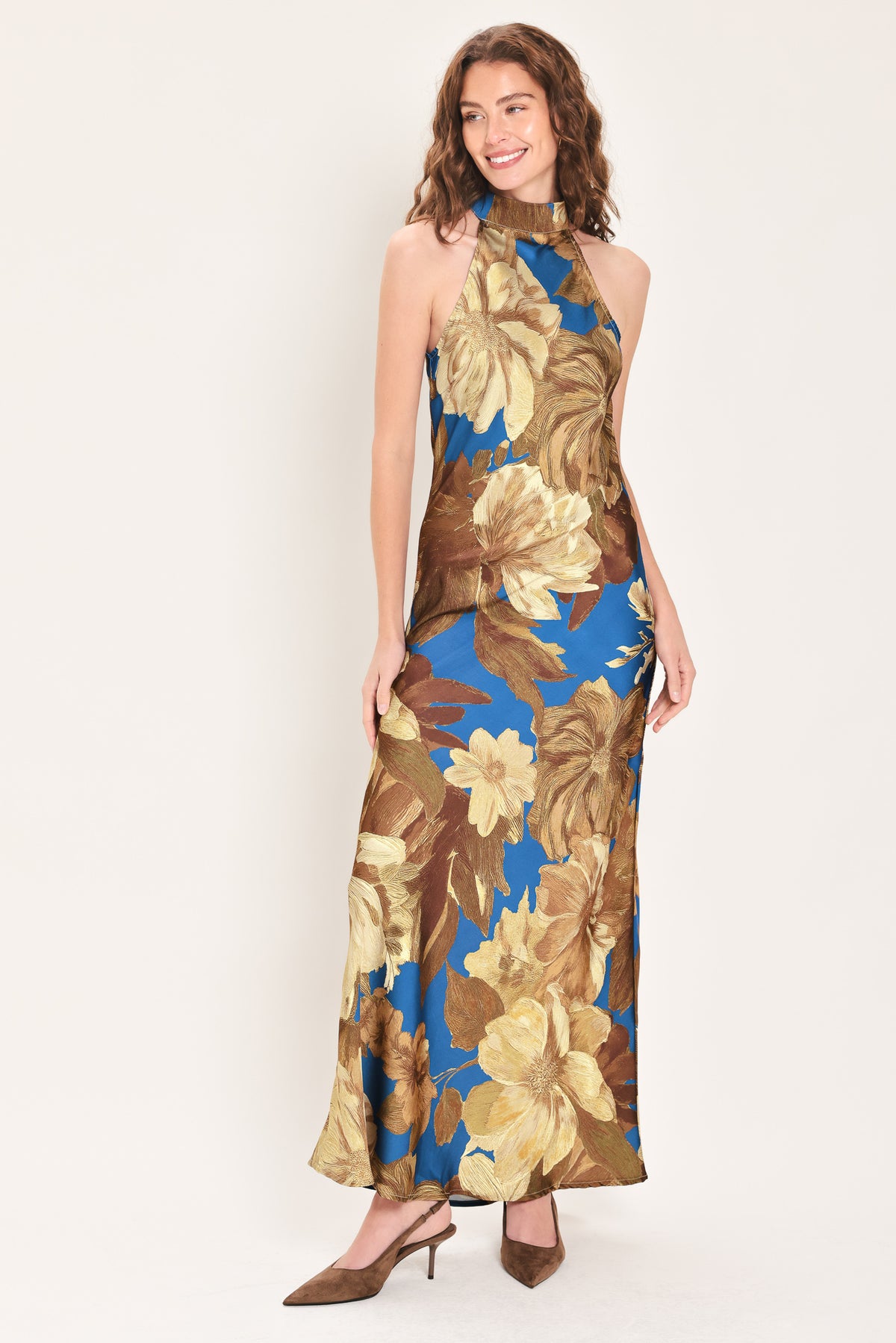 Woman wearing a sleeveless blue satin maxi dress with a mock halter neckline and gold and brown floral pattern | Flying Tomato