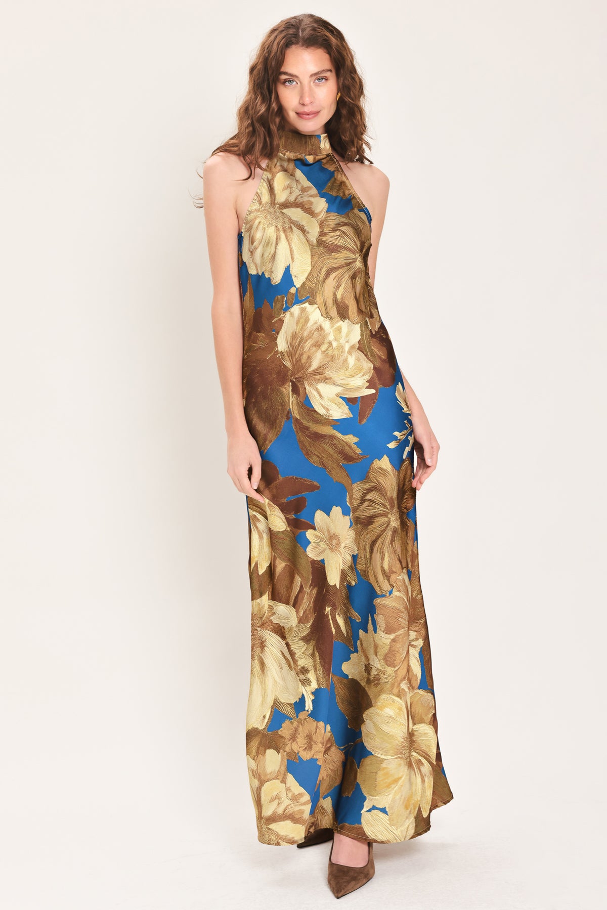 Woman wearing a sleeveless blue satin maxi dress with a mock halter neckline and gold and brown floral pattern | Flying Tomato