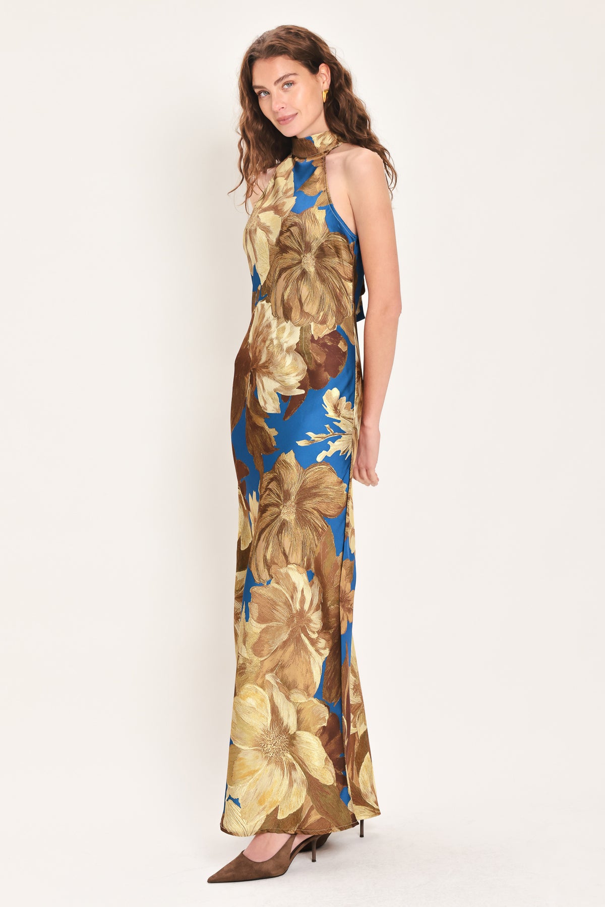 Woman wearing a sleeveless blue satin maxi dress with a mock halter neckline and gold and brown floral pattern | Flying Tomato
