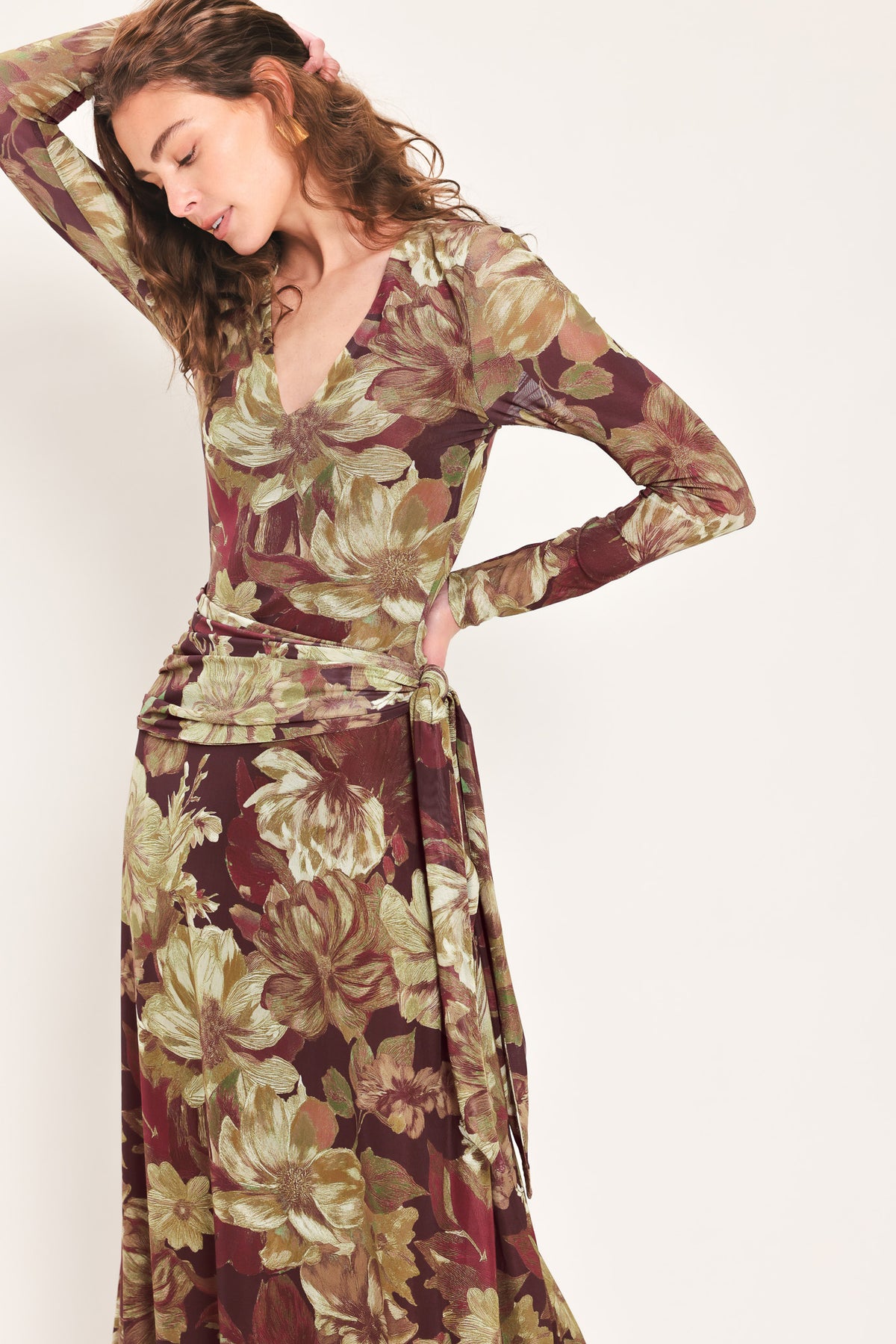 Woman wearing a dark maroon long sleeve mesh maxi dress with brown floral pattern and a waist tie belt that sits right above the hip | Flying Tomato