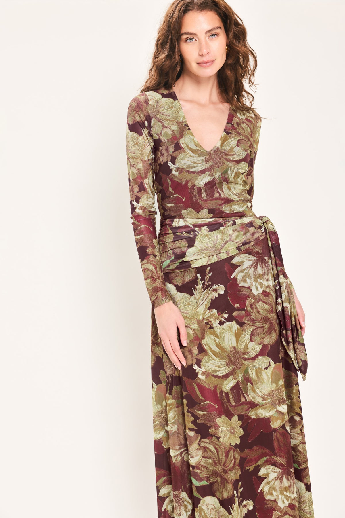 Woman wearing a dark maroon long sleeve mesh maxi dress with brown floral pattern and a waist tie belt that sits right above the hip | Flying Tomato