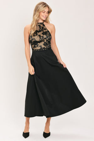 Woman wearing a halter mock neck midid dress with beige top base and black floral lace over and black skirt and black waist belt | Flying Tomato