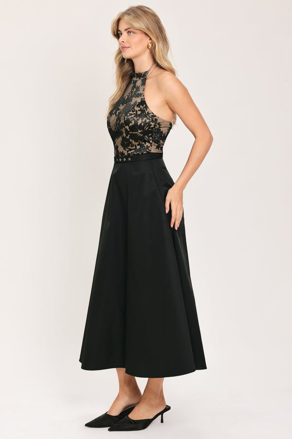 Woman wearing a halter mock neck midid dress with beige top base and black floral lace over and black skirt and black waist belt | Flying Tomato