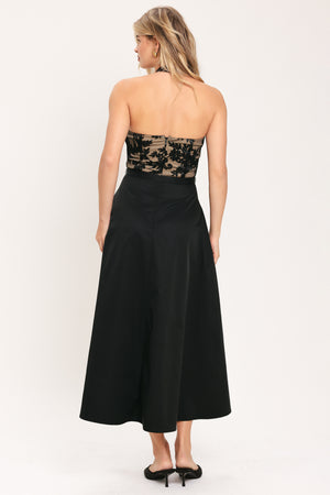 Woman wearing a halter mock neck midid dress with beige top base and black floral lace over and black skirt and black waist belt | Flying Tomato