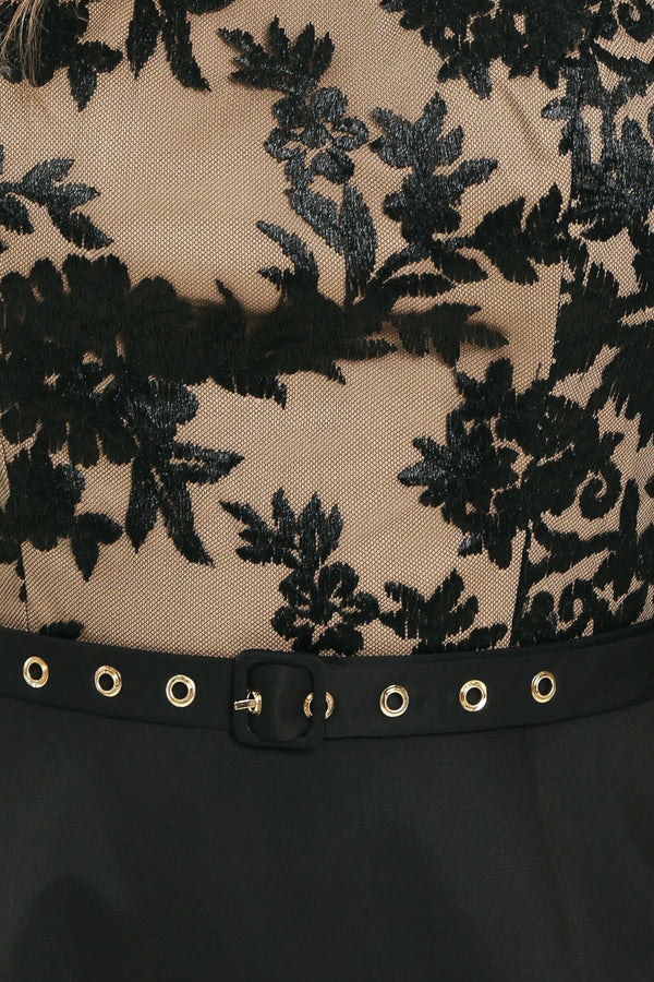 Woman wearing a halter mock neck midid dress with beige top base and black floral lace over and black skirt and black waist belt | Flying Tomato