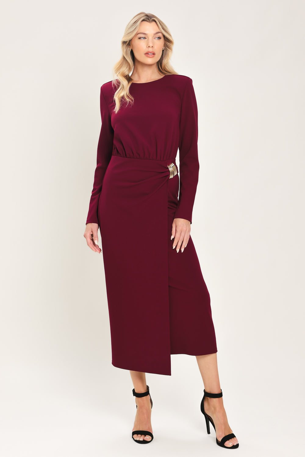 Woman wearing a long sleeve burgundy midi dress with a gold hardware holding slight gathered detailing around the hip | Flying Tomato