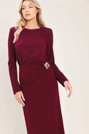 Woman wearing a long sleeve burgundy midi dress with a gold hardware holding slight gathered detailing around the hip | Flying Tomato