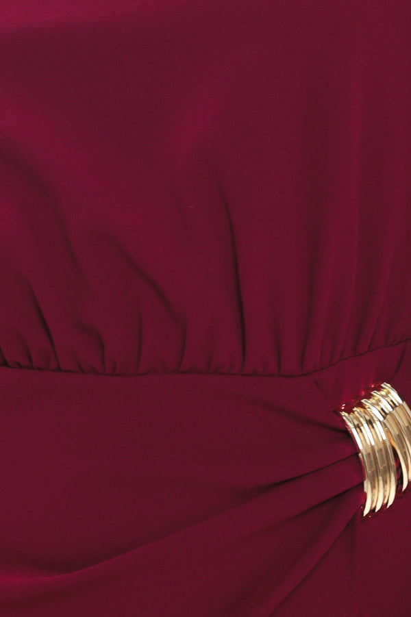 Woman wearing a long sleeve burgundy midi dress with a gold hardware holding slight gathered detailing around the hip | Flying Tomato
