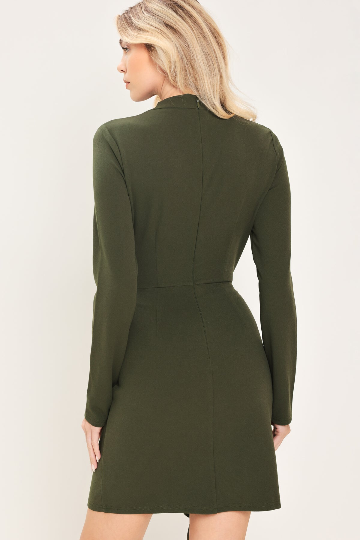 Woman wearing a long sleeve olive green mini dress with gathered fabric around the lower abdomen and fabric draping from a gold hardware a the corner of the waist | Flying Tomato