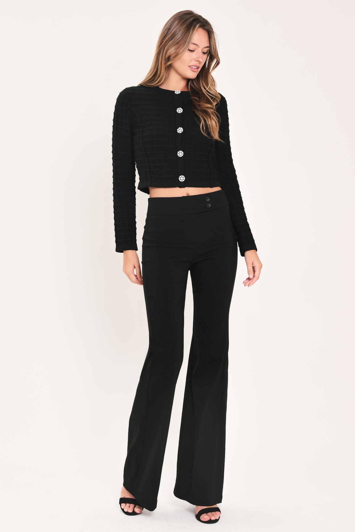 A woman modeling a black textured cropped cardigan with decorative silver buttons down the front | Flying Tomato
