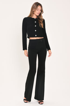 A woman modeling a black textured cropped cardigan with decorative silver buttons down the front | Flying Tomato