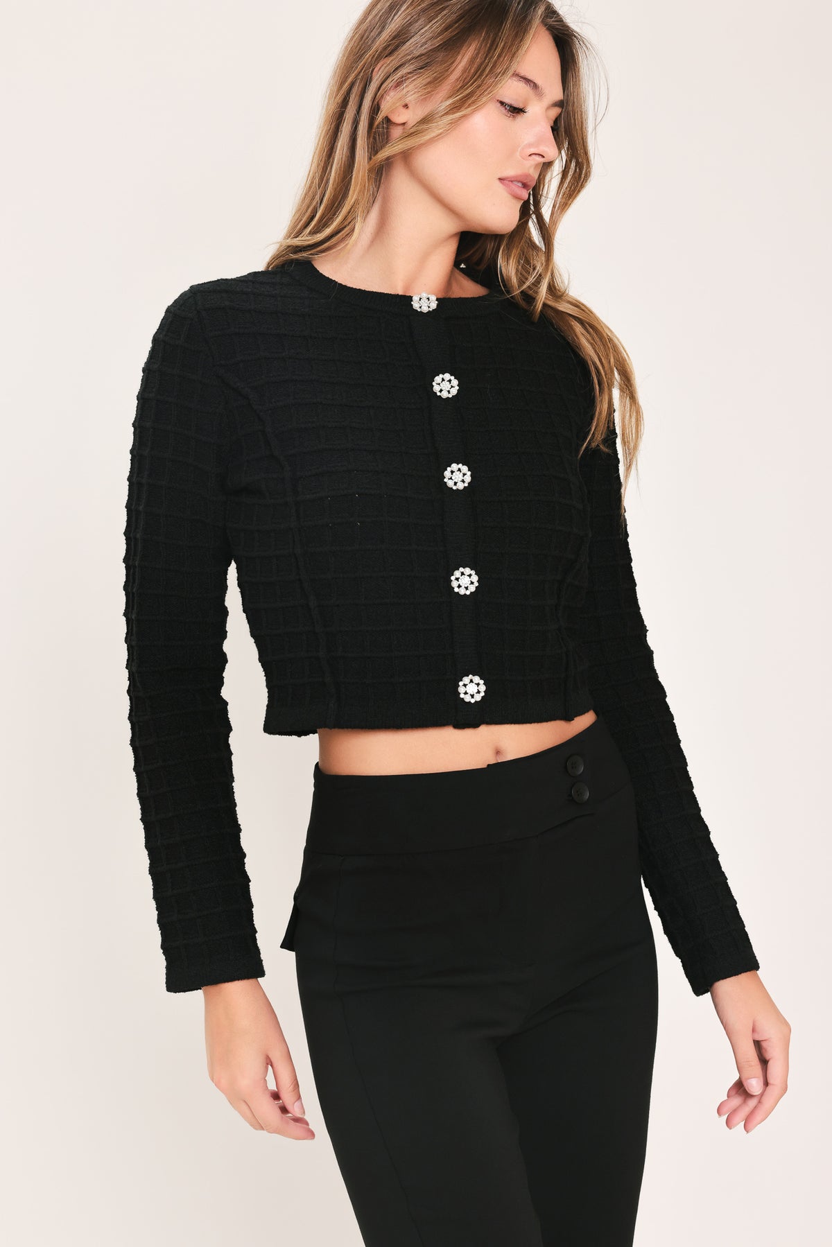 A woman modeling a black textured cropped cardigan with decorative silver buttons down the front | Flying Tomato