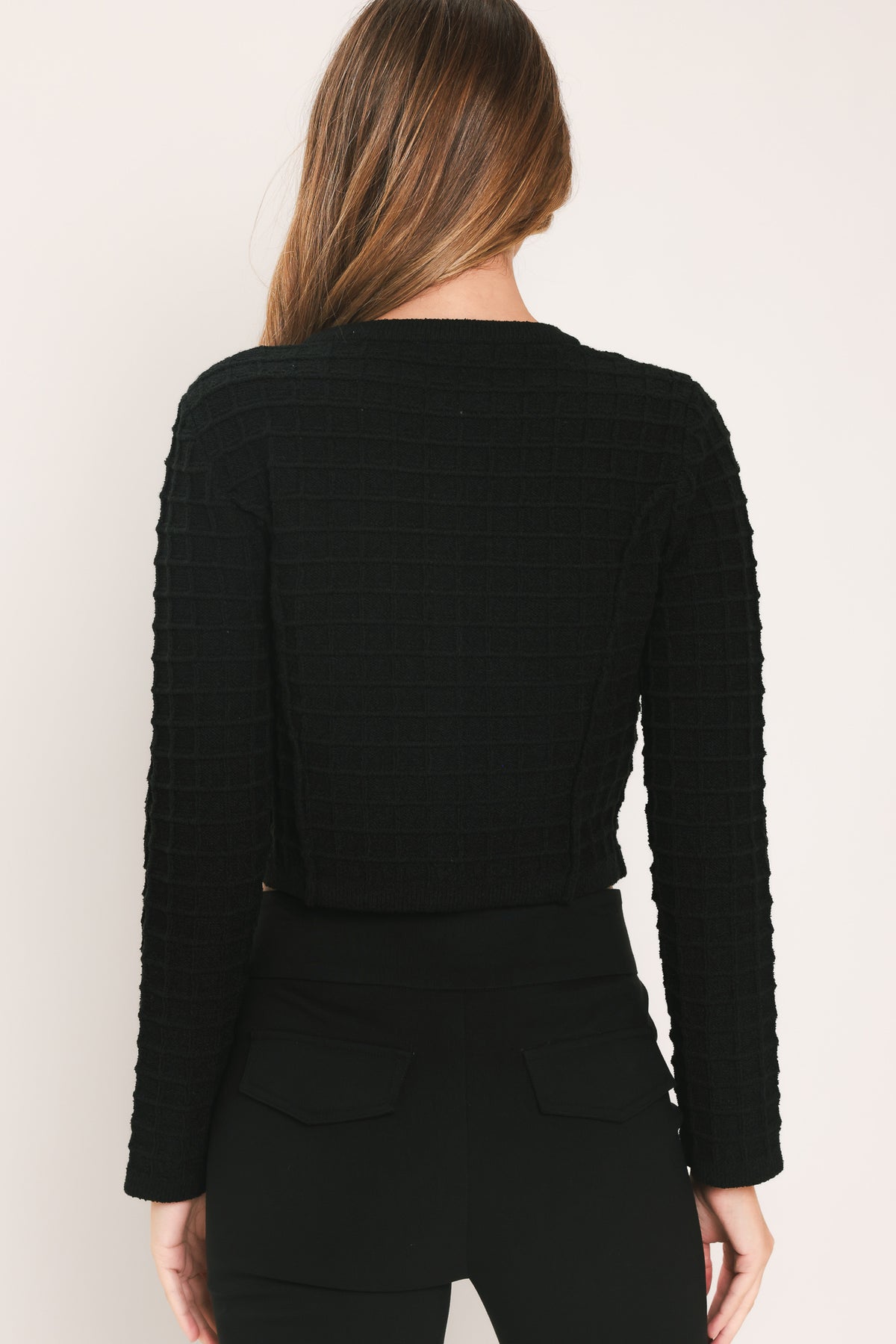 A woman modeling a black textured cropped cardigan with decorative silver buttons down the front | Flying Tomato