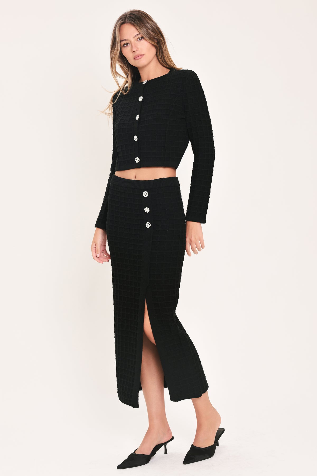 A woman modeling a black textured cropped cardigan with decorative silver buttons down the front | Flying Tomato