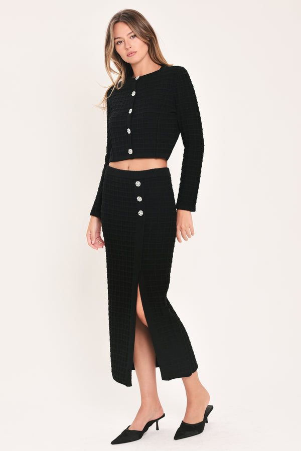 A woman modeling a black textured cropped cardigan with decorative silver buttons down the front | Flying Tomato