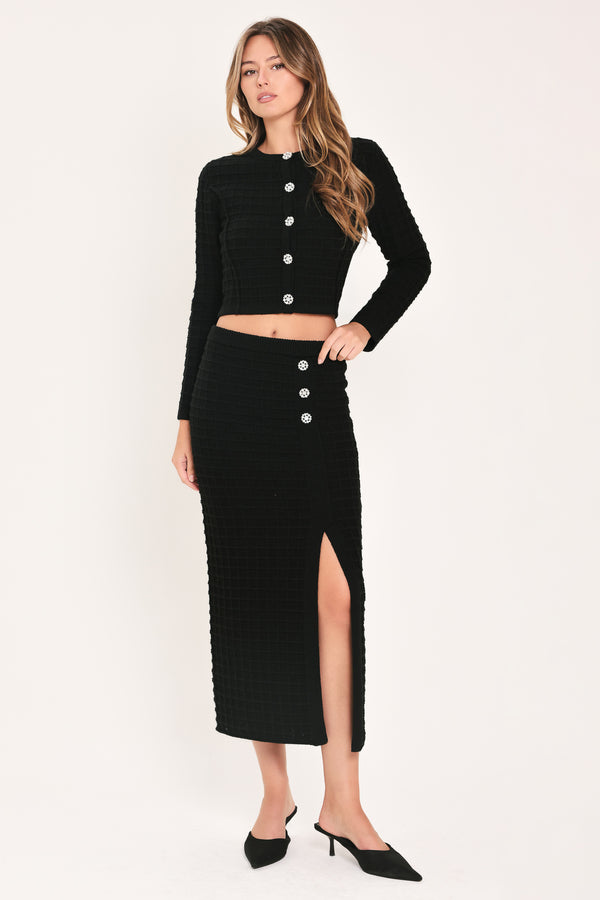 A woman modeling a black textured cropped cardigan with decorative silver buttons down the front | Flying Tomato