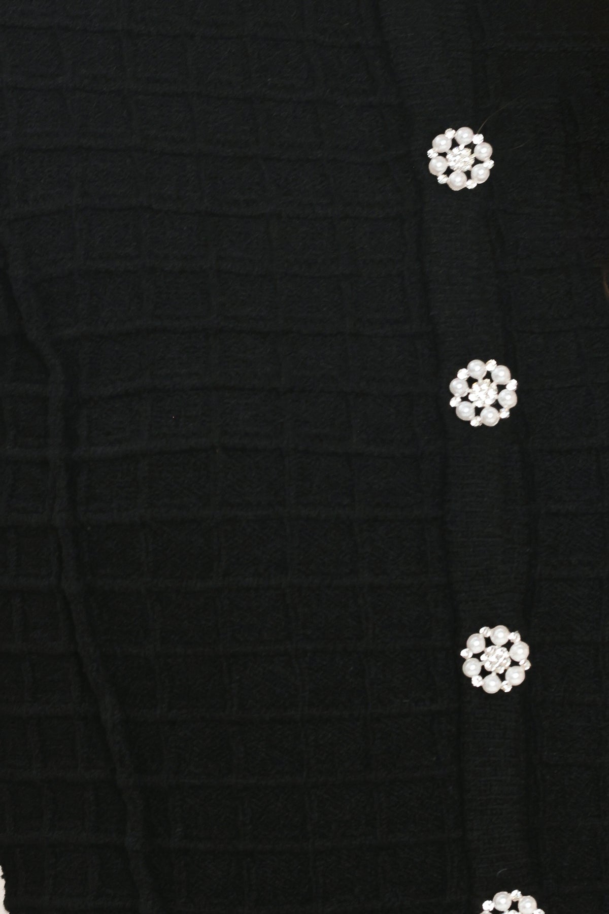 A woman modeling a black textured cropped cardigan with decorative silver buttons down the front | Flying Tomato