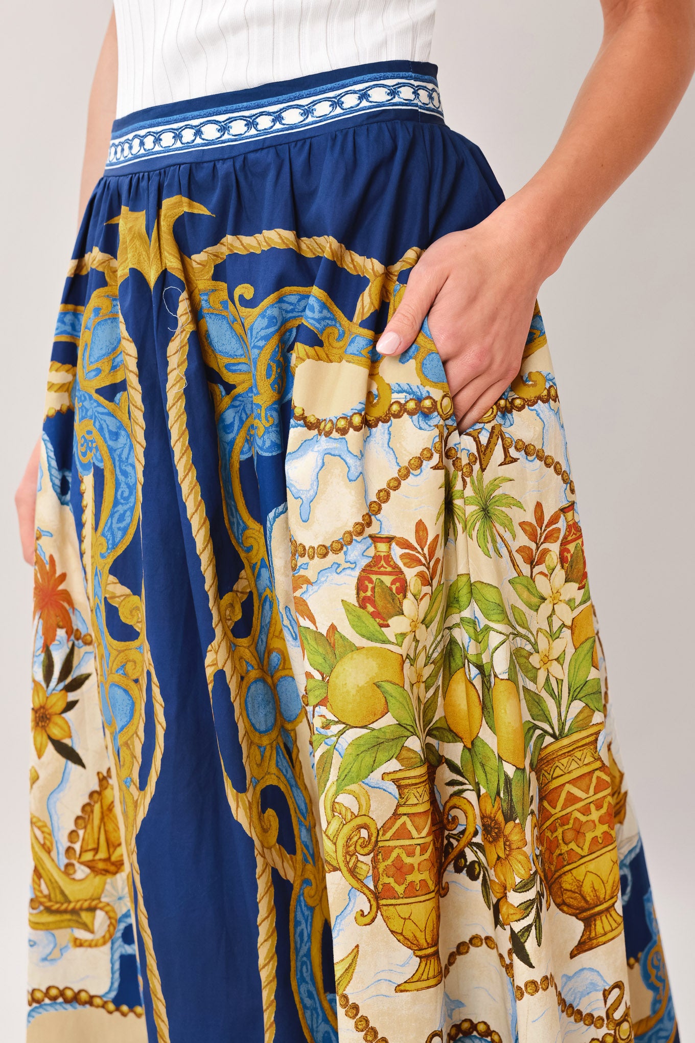 Woman wearing a midi skirt with intricate blue, gold and multicolor pattern, pockets, and side zipper closure | Flying Tomato
