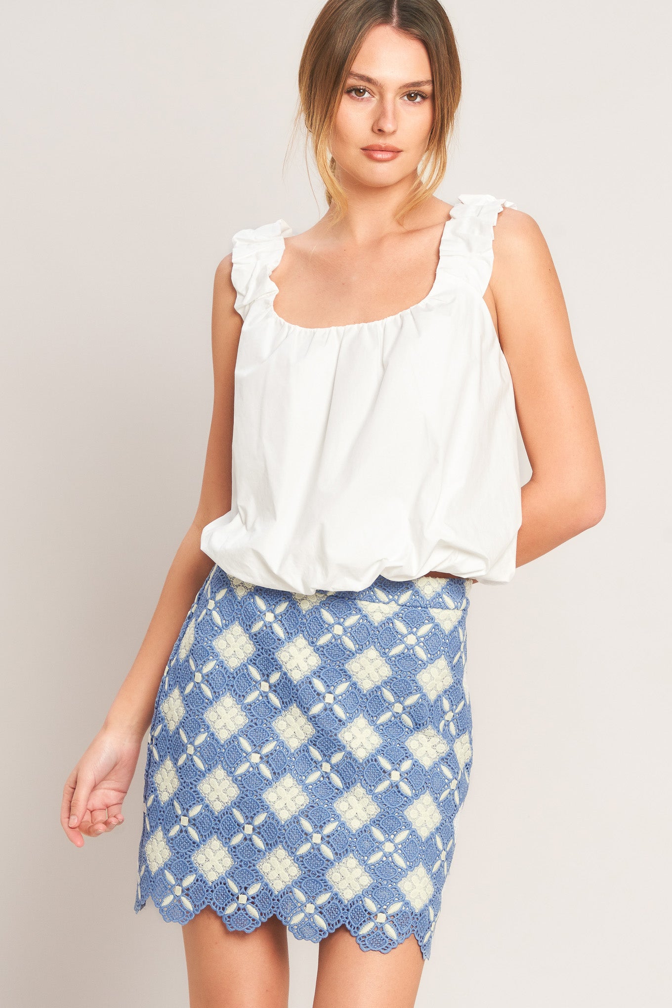 Woman wearing a white top and blue patterned skirt on a plain background