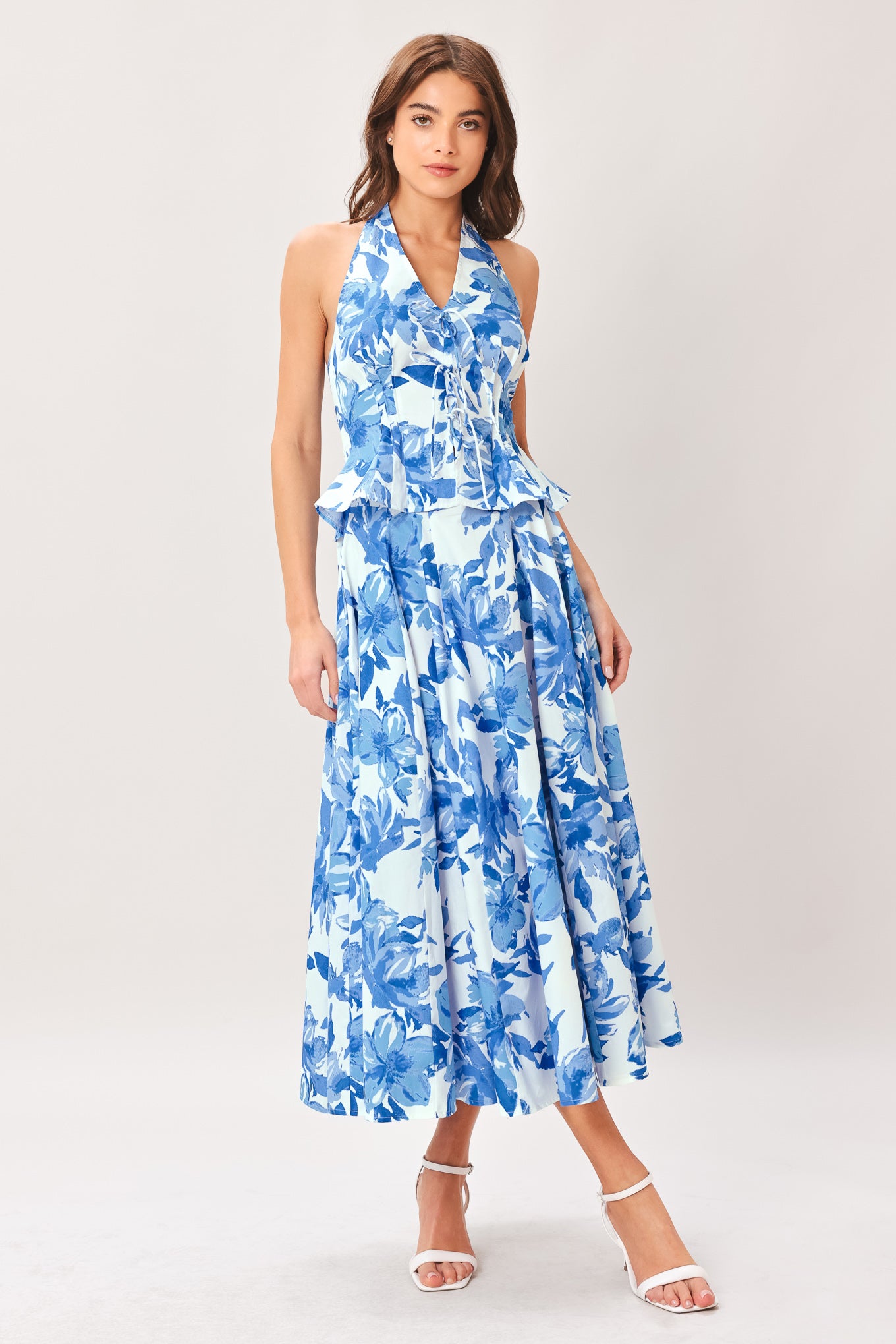Woman wearing a blue floral top and skirt featuring V halter neckline, corset waist, front tie, peplum and back zipper closure | Flying Tomato