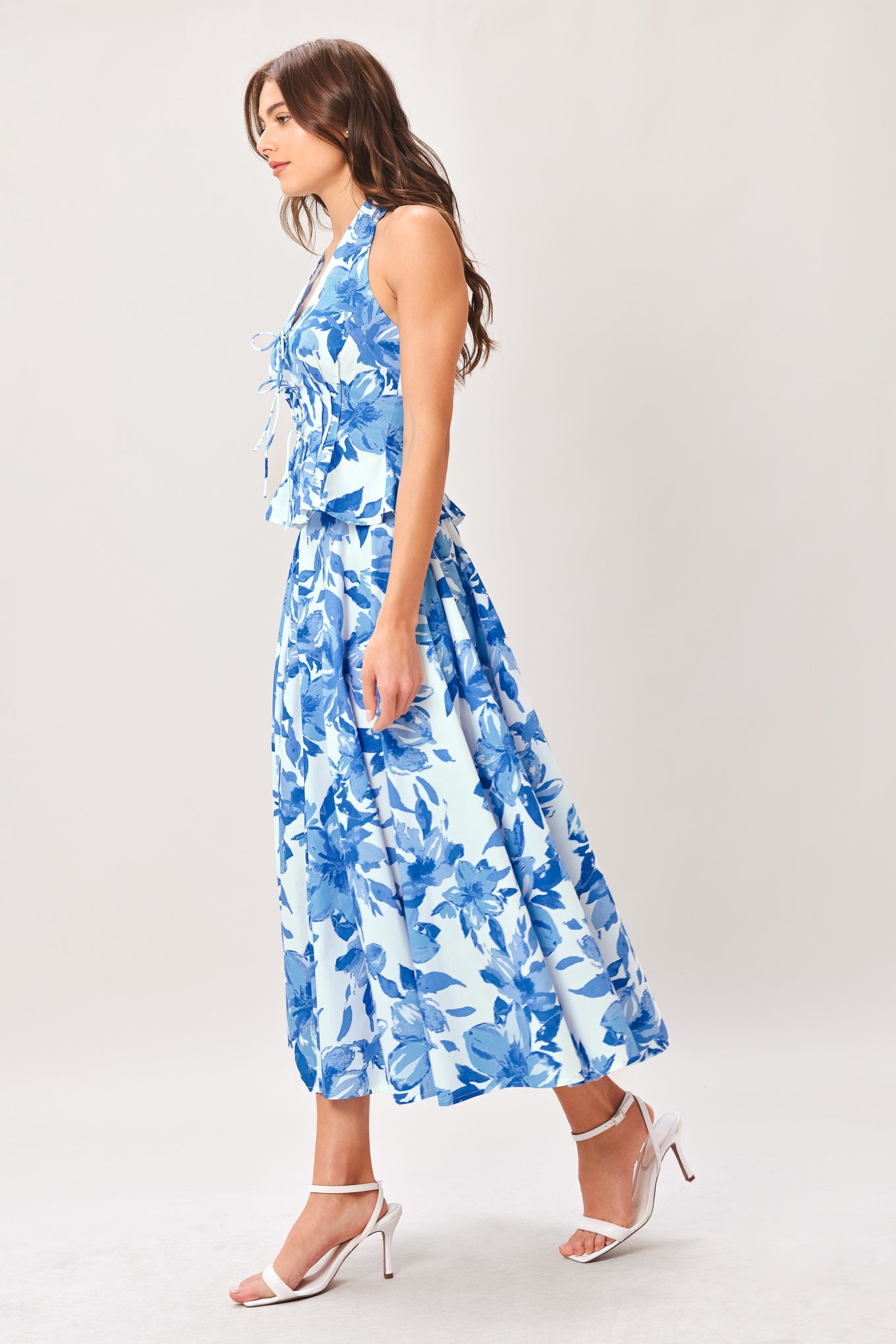 Woman wearing a blue floral top and skirt featuring V halter neckline, corset waist, front tie, peplum and back zipper closure | Flying Tomato