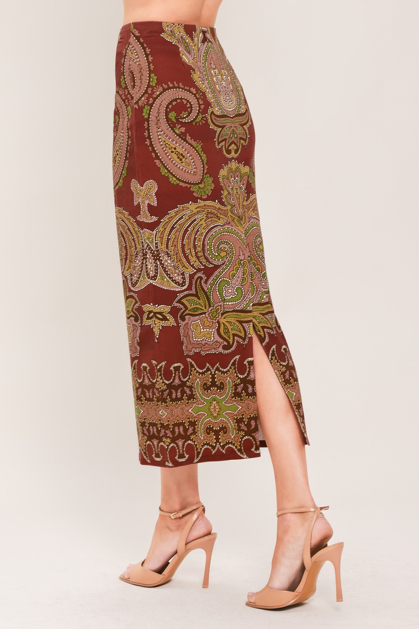 A woman wearing a midi skirt with an ornate paisley pattern in rust red, gold, and olive green | Flying Tomato
