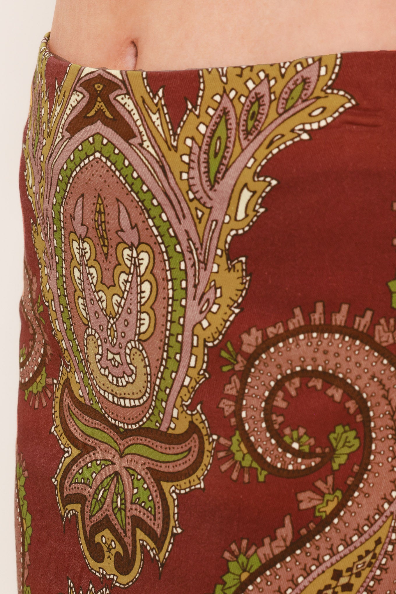 A woman wearing a midi skirt with an ornate paisley pattern in rust red, gold, and olive green | Flying Tomato
