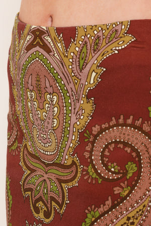 A woman wearing a midi skirt with an ornate paisley pattern in rust red, gold, and olive green | Flying Tomato