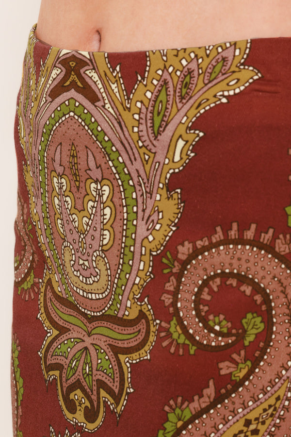 A woman wearing a midi skirt with an ornate paisley pattern in rust red, gold, and olive green | Flying Tomato