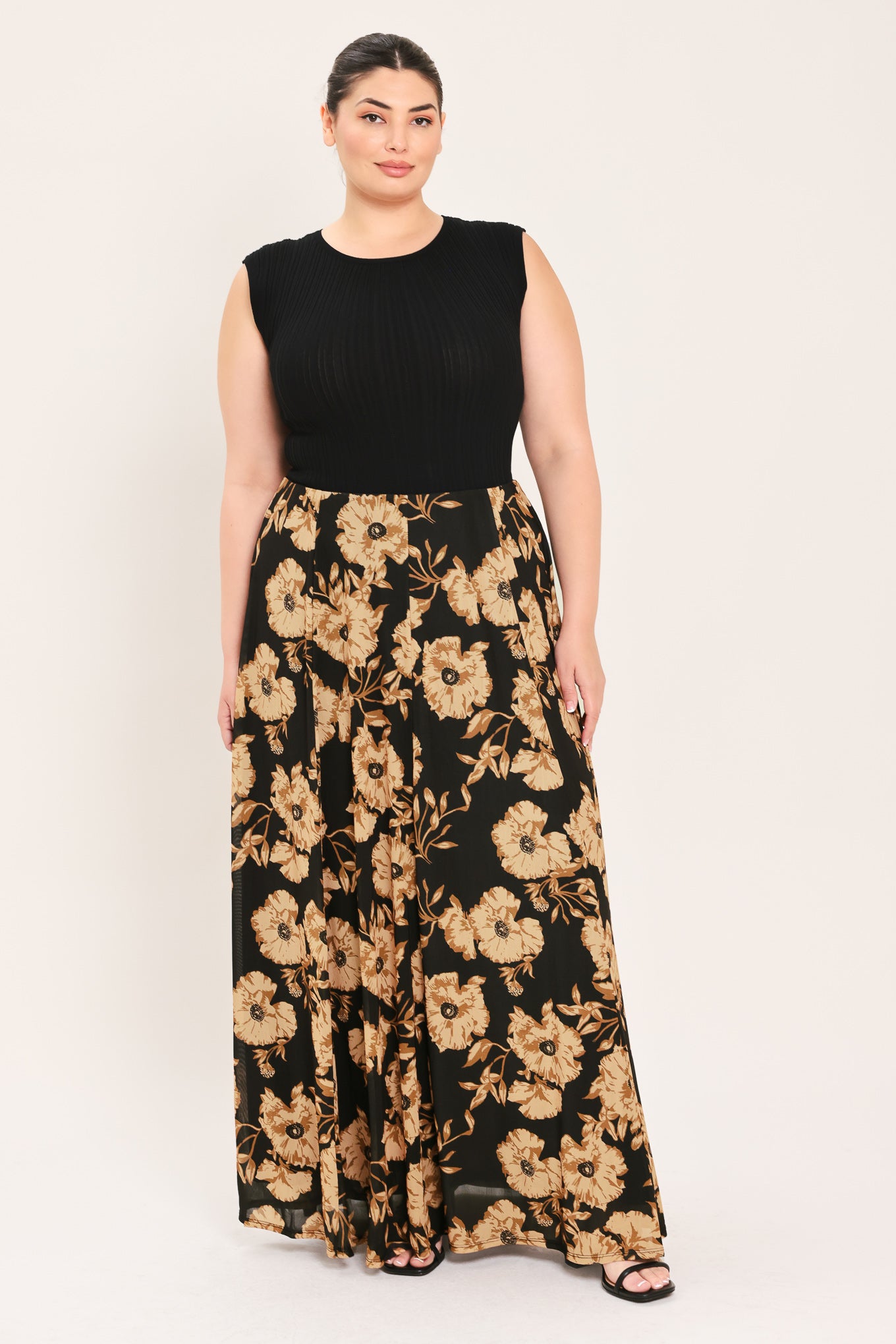 A woman modeling a sleeveless black top paired with a long black skirt featuring a large beige floral print | Plus Curve Flying Tomato
