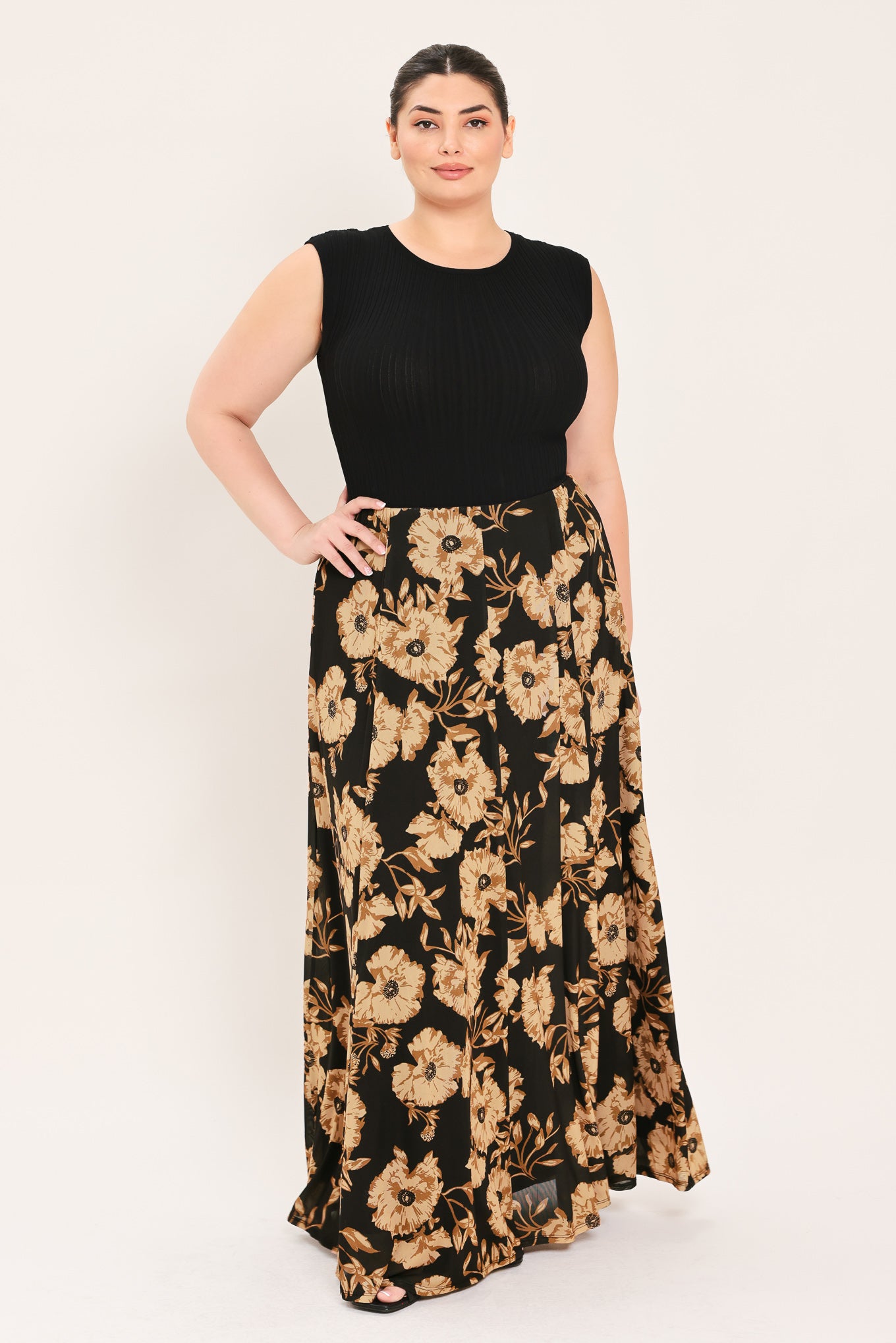 A woman modeling a sleeveless black top paired with a long black skirt featuring a large beige floral print | Plus Curve Flying Tomato