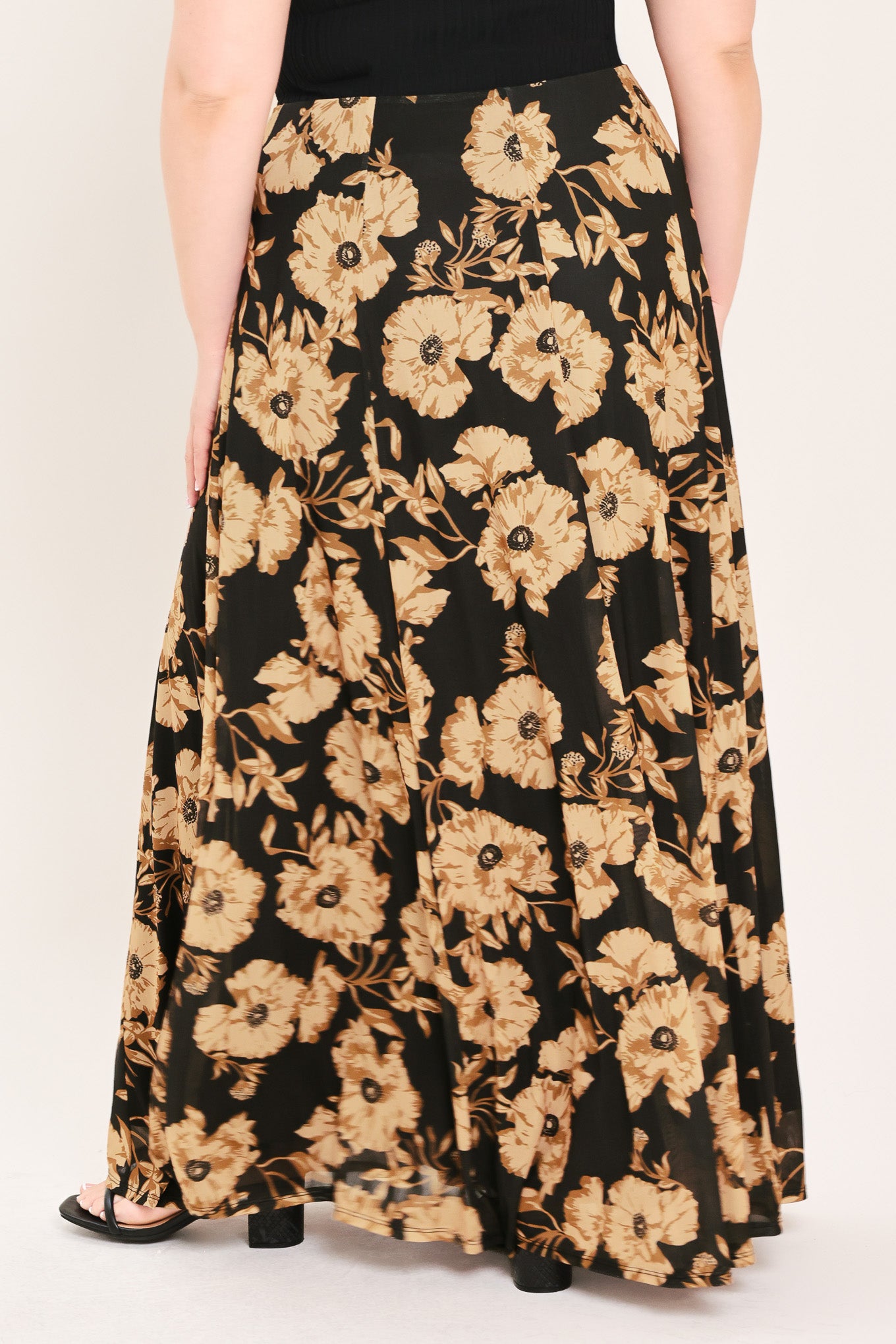 A woman modeling a sleeveless black top paired with a long black skirt featuring a large beige floral print | Plus Curve Flying Tomato