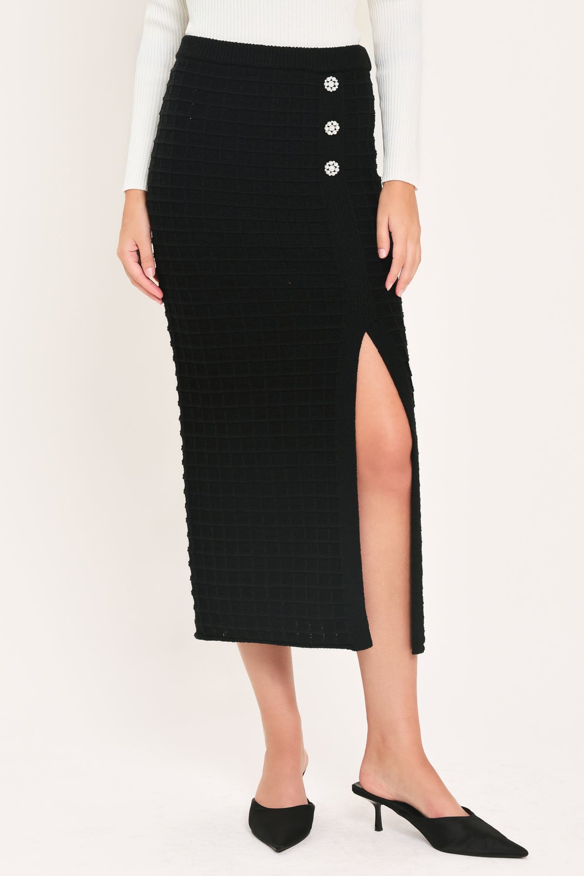 A black textured midi skirt with a front slit and three decorative silver buttons, worn by a model | Flying Tomato