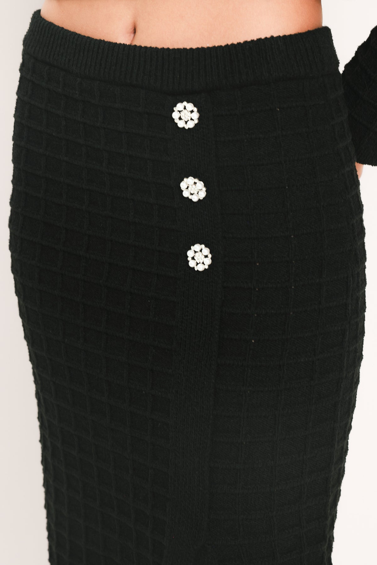 A black textured midi skirt with a front slit and three decorative silver buttons, worn by a model | Flying Tomato