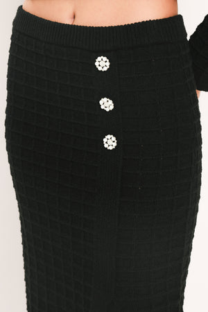 A black textured midi skirt with a front slit and three decorative silver buttons, worn by a model | Flying Tomato