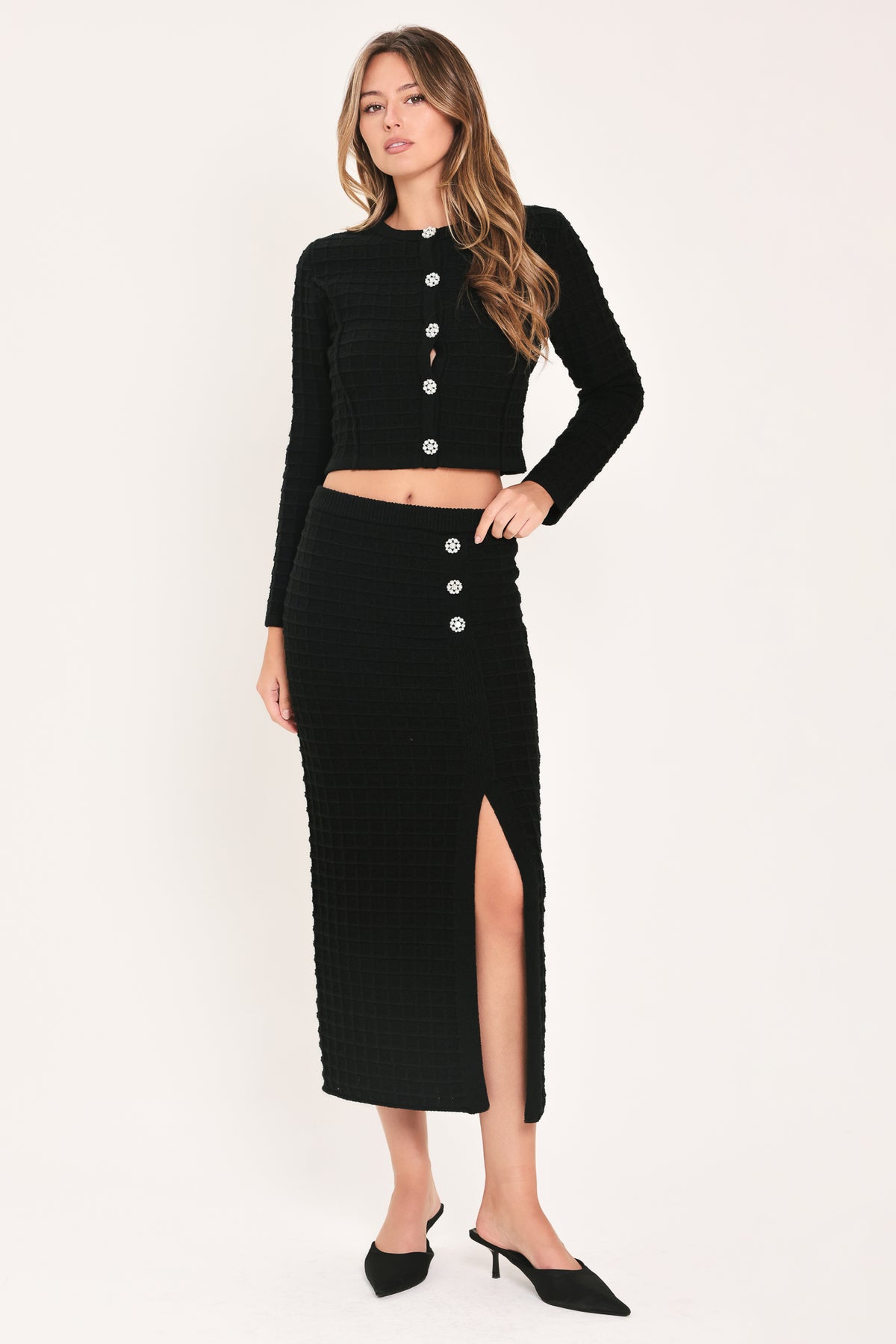 A black textured midi skirt with a front slit and three decorative silver buttons, worn by a model | Flying Tomato
