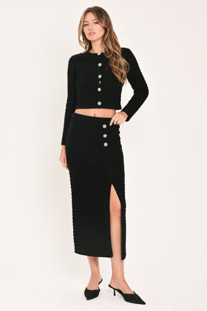 A black textured midi skirt with a front slit and three decorative silver buttons, worn by a model | Flying Tomato