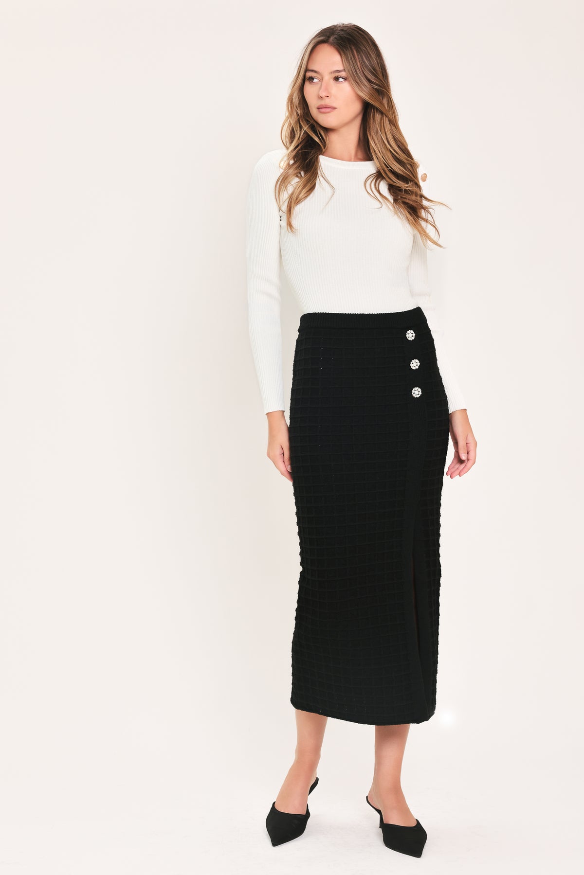 A black textured midi skirt with a front slit and three decorative silver buttons, worn by a model | Flying Tomato