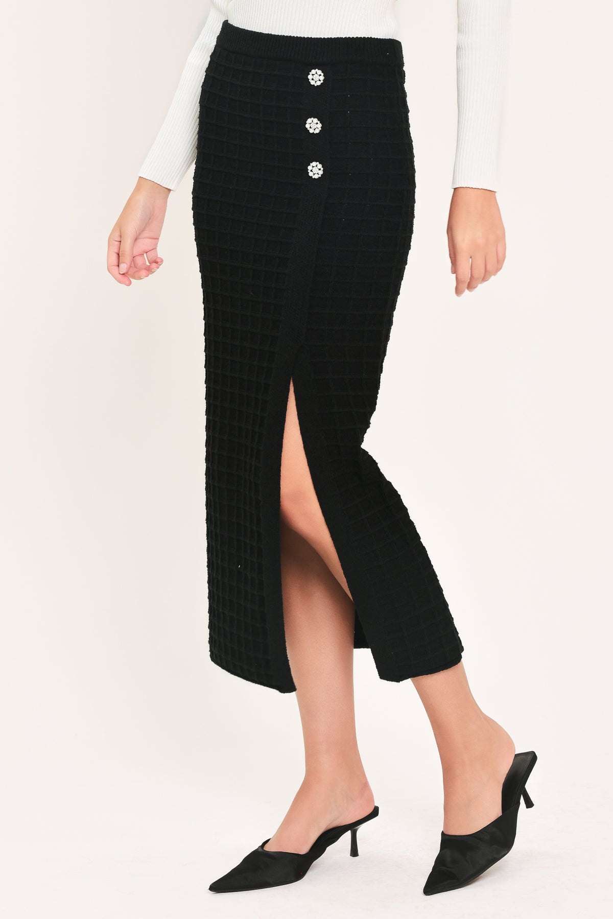 A black textured midi skirt with a front slit and three decorative silver buttons, worn by a model | Flying Tomato